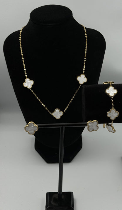 standaard“Mizori Jewelry white and gold stainless steel clover jewelry set displayed on a stand, including earrings, bracelet, and necklace, elegant and minimalist design.